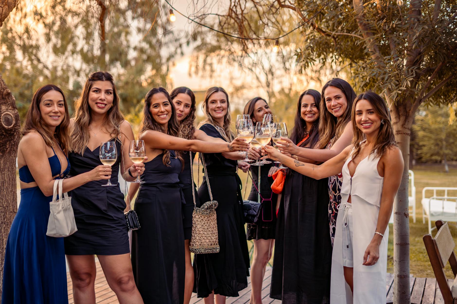 A group of women enjoying a celebratory toast outdoors at sunset in stylish dresses